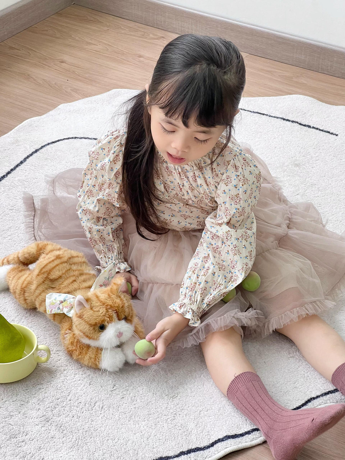  Sweet little girl playing with realistic fluffy orange tabby cat stuffed animal on cozy white rug, cute kids play scene with plush kitty toy