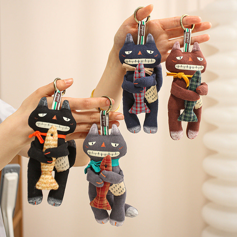 Various colorful handmade black cat bag charms holding small fish hanging from hands