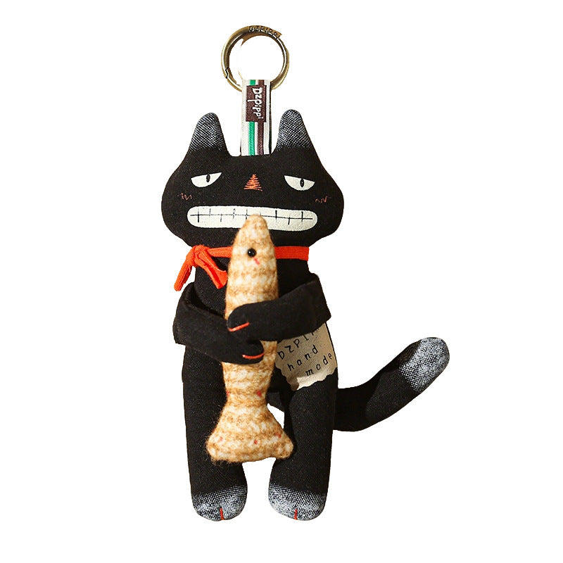 Cute black cat bag charm holding a fish with a golden keyring on white background
