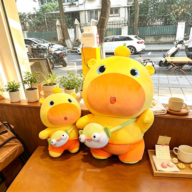 Large and small yellow‑orange capybara stuffed plush by cafe window, real‑life display